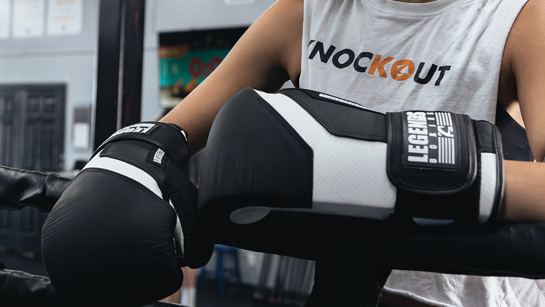 Woman in a gym wearing boxing gloves and a 'Knockout' tank top.